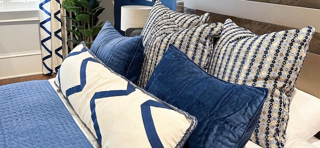 A set of pillows arrange in a decorative fashion. They sit atop a large mattress. The pillows are primarily blue and white.