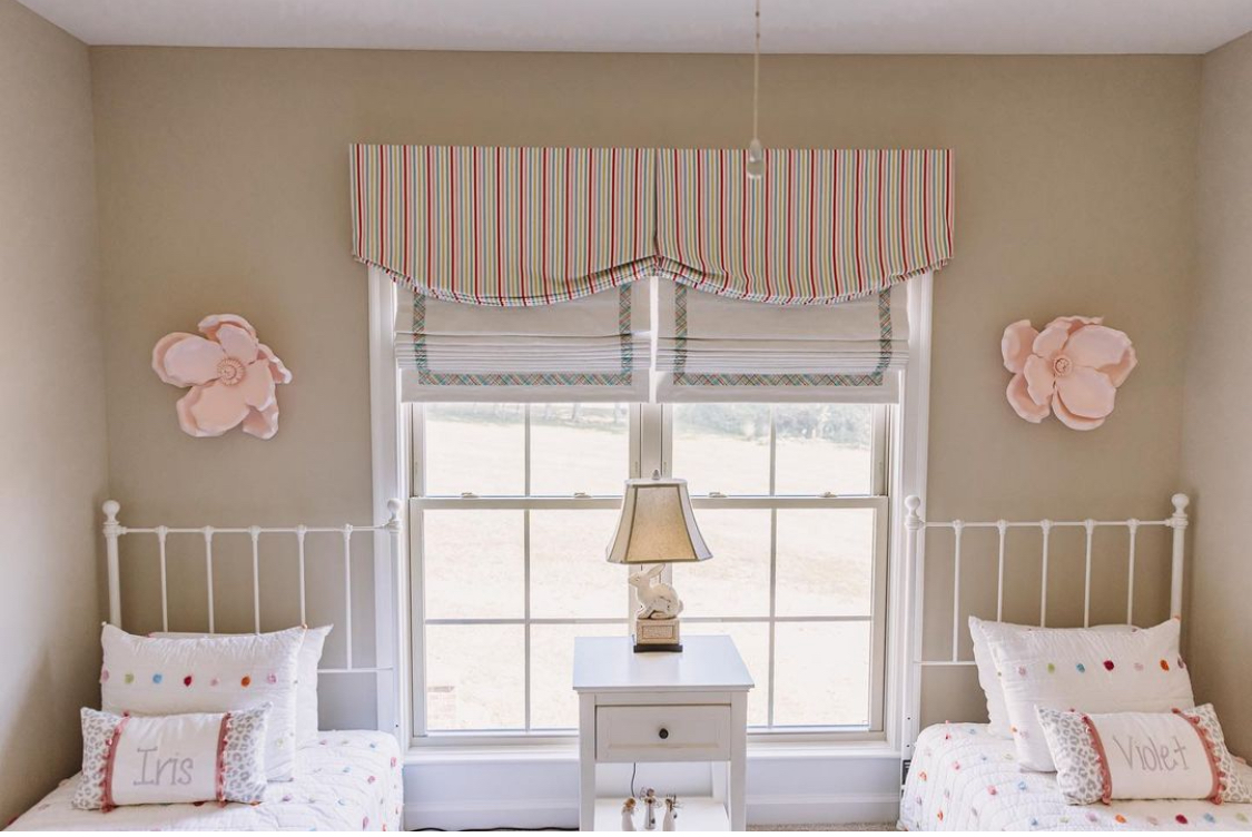 Valances decorating the top of a window in a bedroom. There are two separate beds in the room.