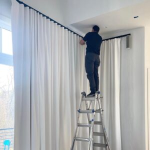 Professional installer putting up custom drapes inside a home. The drapes are white.
