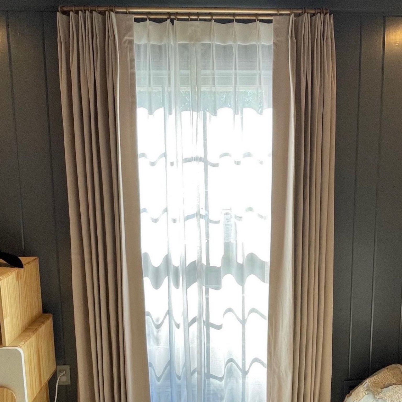 A sheer curtain covering a window. Sunlight is visible through the curtain and it is positioned underneath another type of window treatment.