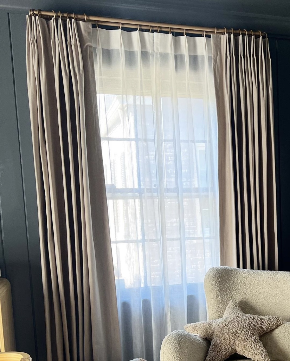 A sheer curtain covering a room window. It is layered beneath another window treatment.
